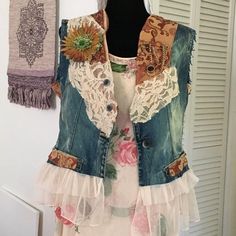 a woman's jean vest with sunflowers and lace on the back, hanging from a hook