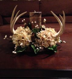 flowers and antlers are arranged on a table in front of a couch with a wooden block