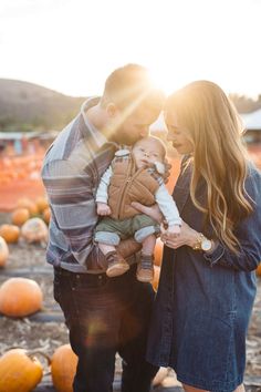 a man and woman holding a baby in front of pumpkins