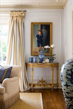 a living room with a painting on the wall next to a chair and table in front of a window