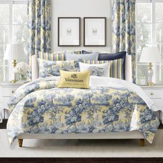 a bedroom with yellow and blue bedding, white walls and curtains on the windowsill