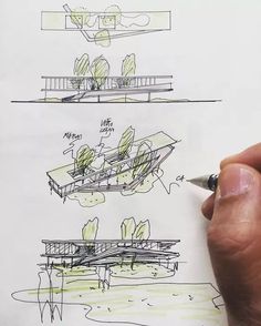 a hand is holding a pen and drawing plans for a building with trees on it