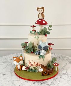 a three tiered cake decorated with woodland animals and mushrooms is on a marble table