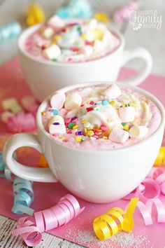 two cups filled with marshmallows and sprinkles on top of pink paper