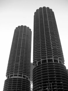 two very tall buildings next to each other in black and white photo with the sky behind them