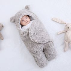 a baby in a bunny costume laying next to three stuffed animals on a white blanket