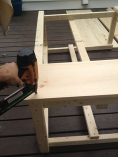 a person using a power drill to attach the back end of a wooden bench on a deck