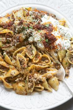 a white plate topped with pasta and meat covered in sauce, parmesan cheese