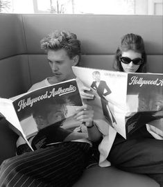 two people are sitting on a couch reading hollywood movie posters, one is wearing sunglasses and the other has his hair pulled back