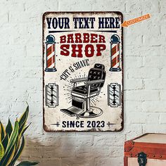 a barber shop sign hanging on the wall next to a potted plant and suitcase