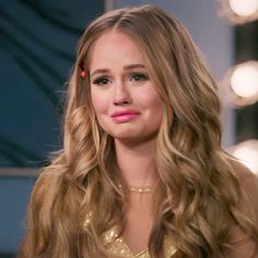 a close up of a person with long hair wearing a gold dress and pink lipstick