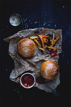 two burgers with fries and ketchup on a piece of wax paper next to dipping sauce