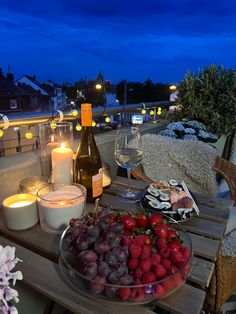 a table topped with a bowl of fruit next to a bottle of wine and candles