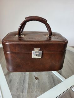 a brown leather suitcase sitting on top of a glass table in front of a white wall