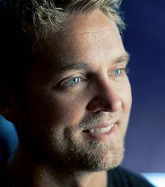 a close up of a person wearing a black shirt and smiling at the camera with blue eyes