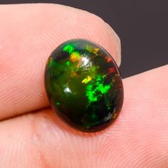 a black opal with green and yellow speckles on it's finger