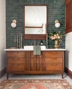 a bathroom with green tiles and wooden cabinets in the corner, along with a rug on the floor