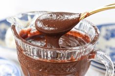 a spoon full of chocolate sauce on top of a glass mug with another cup in the background