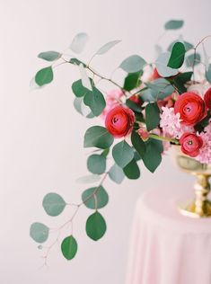 a vase filled with flowers and greenery on top of a pink cloth covered table