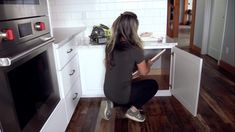 a woman kneeling down in front of an oven with her hand on the door handle