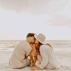 a man and woman kissing while sitting on the sand at the beach with their baby