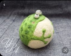 a green and white ball sitting on top of a blue cloth covered surface with two eyes