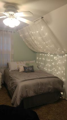 a bed sitting under a window covered in white lights