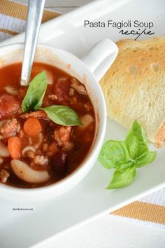 a white plate topped with a bowl of soup next to a piece of bread on top of a table