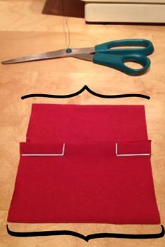 a pair of scissors sitting on top of a piece of red fabric next to a sewing needle