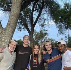 a group of young people standing next to each other under a tree in a park