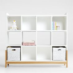 a white book shelf with baskets and books on the top, in front of a white wall