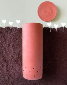 a pink vase sitting on top of dirt next to a red plate and some white hearts