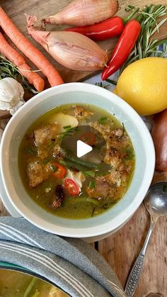 a white bowl filled with soup next to lemons, carrots and other vegetables