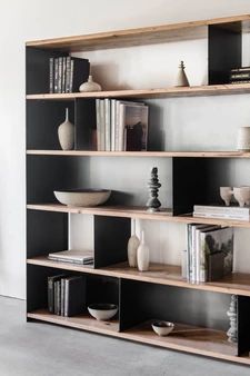 a book shelf filled with books and vases on top of each other in front of a white wall