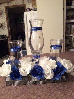 blue and white flowers sit on a counter in front of a glass vase with two glasses next to it