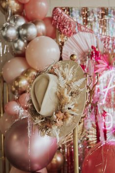 there are many balloons and hats on the wall in front of this display with pink, gold, and silver decorations