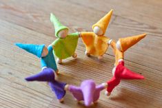 four small wooden toy people standing in a circle on top of a wooden table with one person holding the other's hand