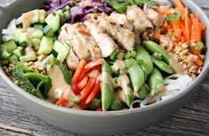 a bowl filled with meat, veggies and dressing on top of a wooden table