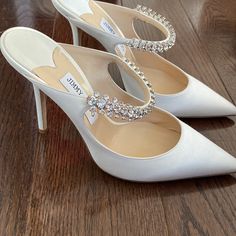 white wedding shoes with jeweled straps on the toes and heels are sitting on a wooden floor