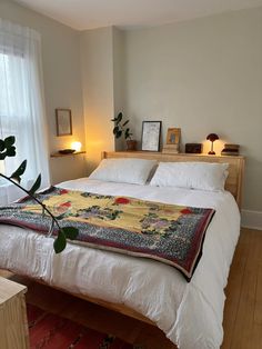 a bed with white linens and pillows in a bedroom next to a window filled with potted plants