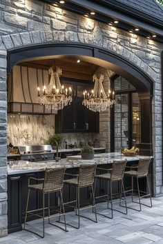 an outdoor kitchen with chandeliers hanging from it's ceiling and stone walls