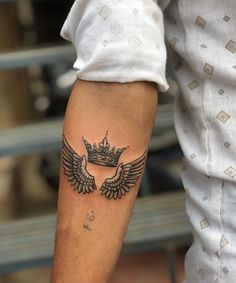 a man's arm with a crown and wings tattoo on the left side of his arm