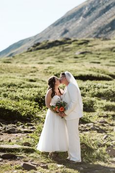 a bride and groom kissing on the side of a hill with mountains in the background