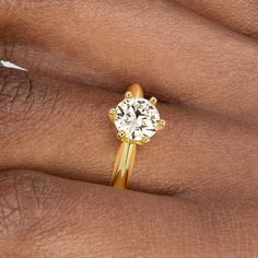 a woman's hand with a yellow gold ring on her finger and a white diamond in the middle