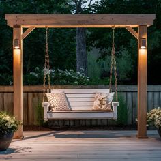 a porch swing is lit up with lights and pillows on the back deck, along with potted plants