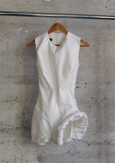 a white bodysuit hanging on a wooden hanger in front of a concrete wall