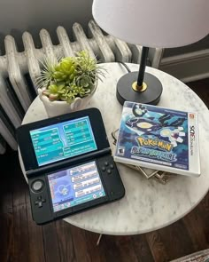 a table topped with two nintendo wii game consoles next to a lamp and a plant