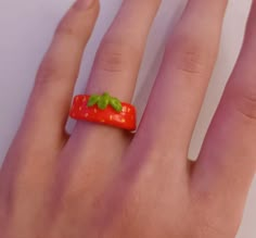 a person's hand with a ring made to look like a strawberry on it