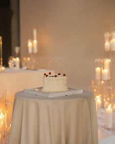 a small white cake sitting on top of a table next to many lit up candles