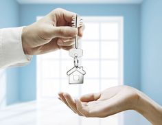 two hands holding keys to each other in front of a house shaped keychain